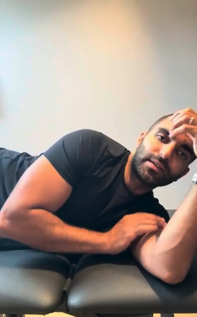 Aziz Youssef, allongé sur sa table, montre la position d'un exercice d'épaule dans la vidéo de démonstration qu'il joint à sa prescription